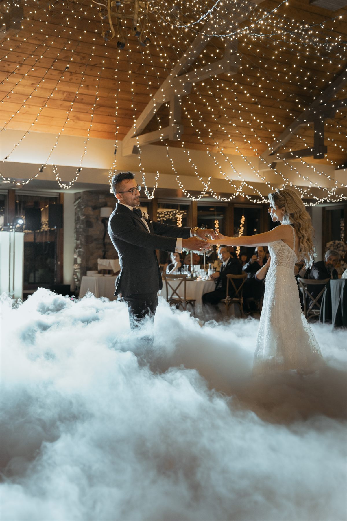 First dance on a cloud of fog beneath string lights