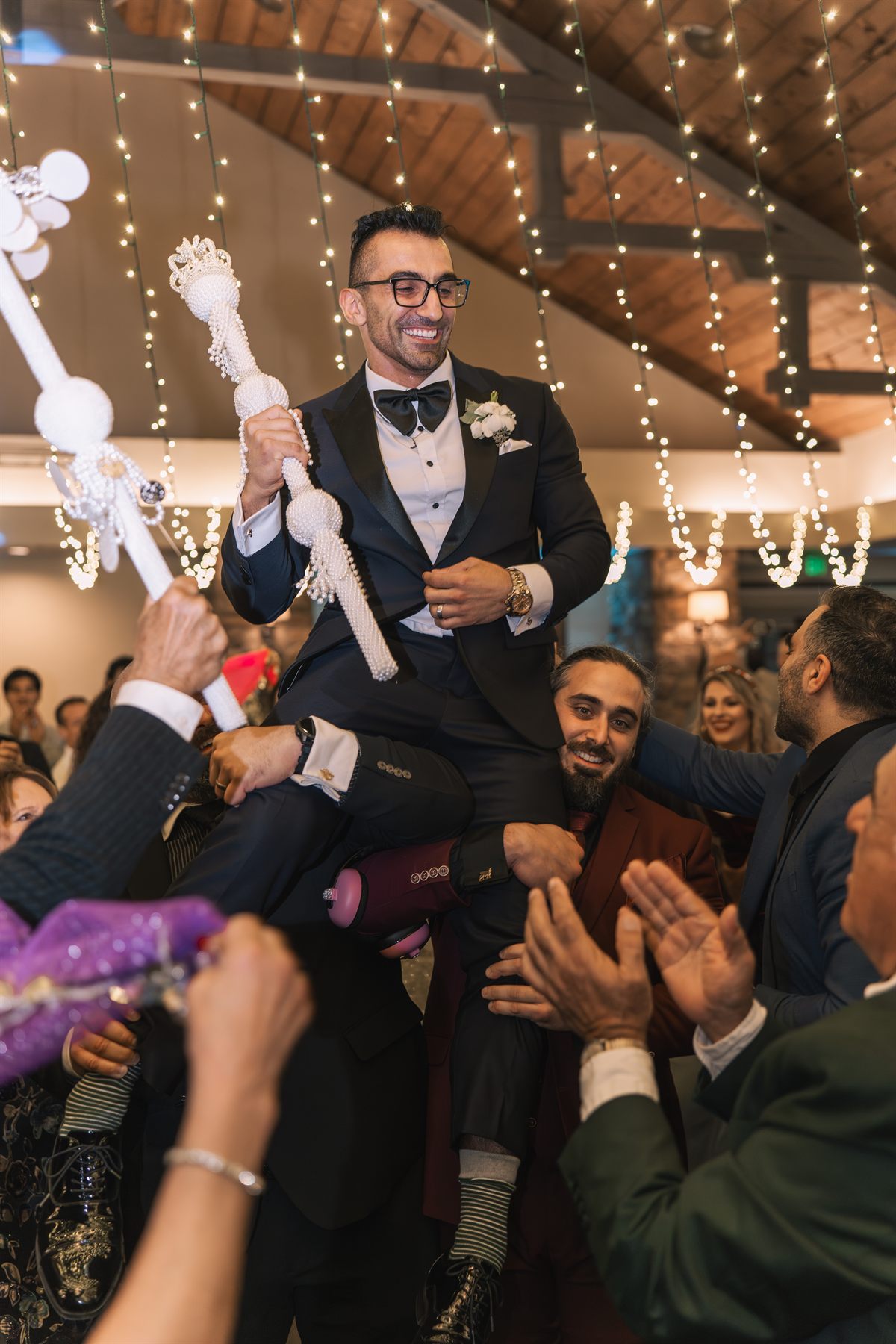 Groom lifted on shoulders during reception dancing, guests clapping around him