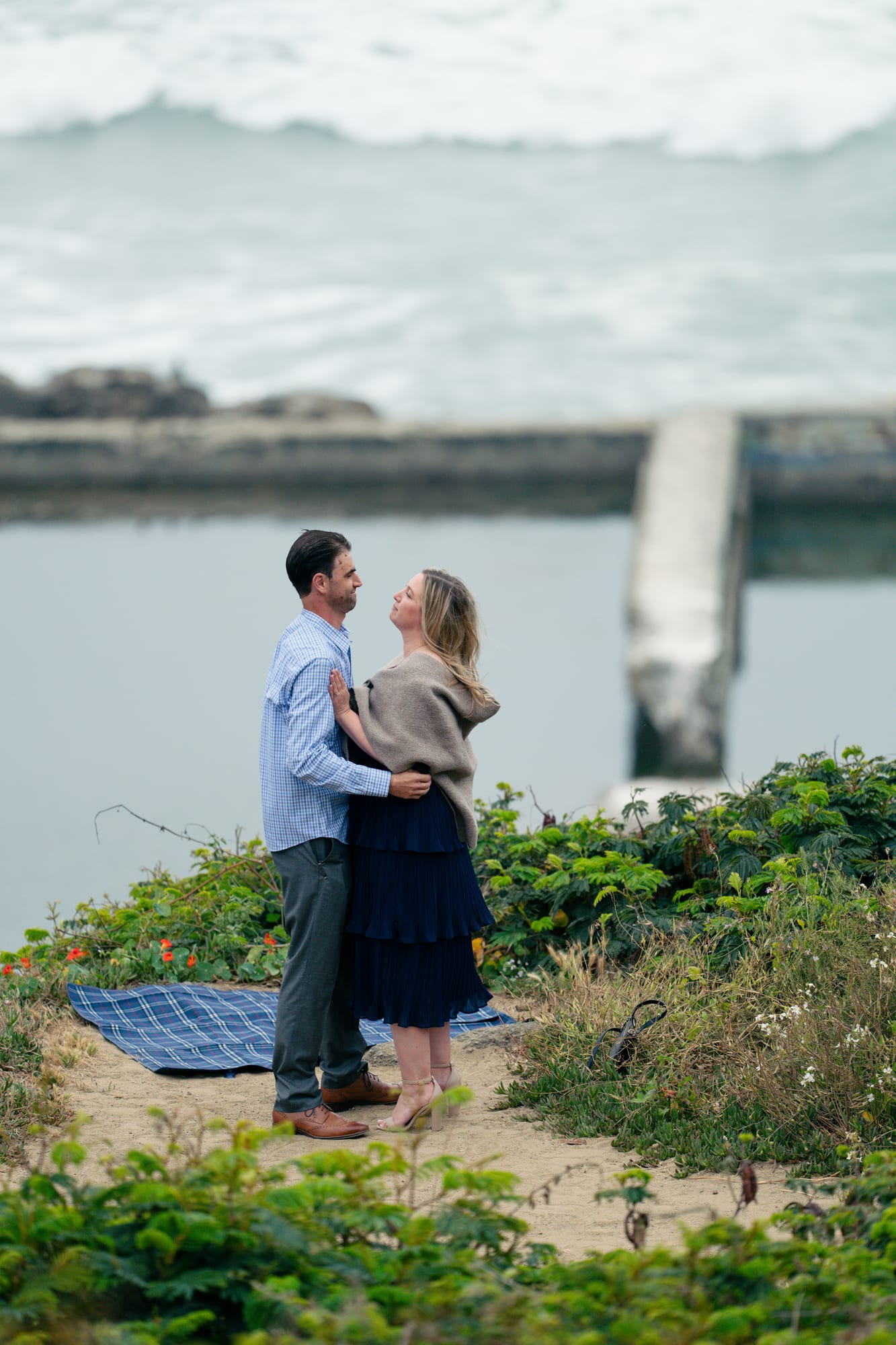 Couple embracing face to face on the cliffside path, a concrete piling and the fogged-in ocean behind them