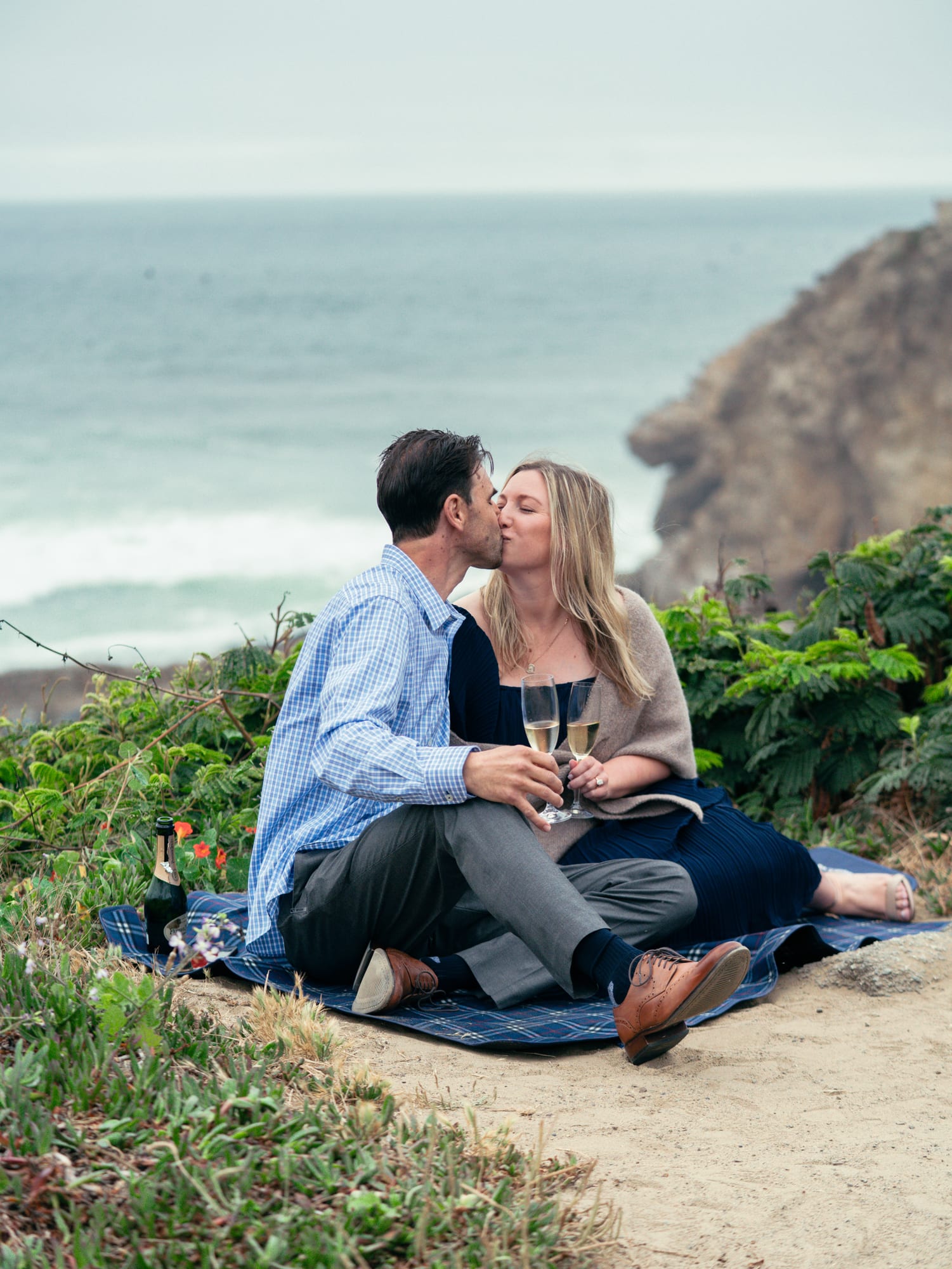 Close portrait of the couple cheek to cheek, she holds two champagne flutes and smiles past the camera