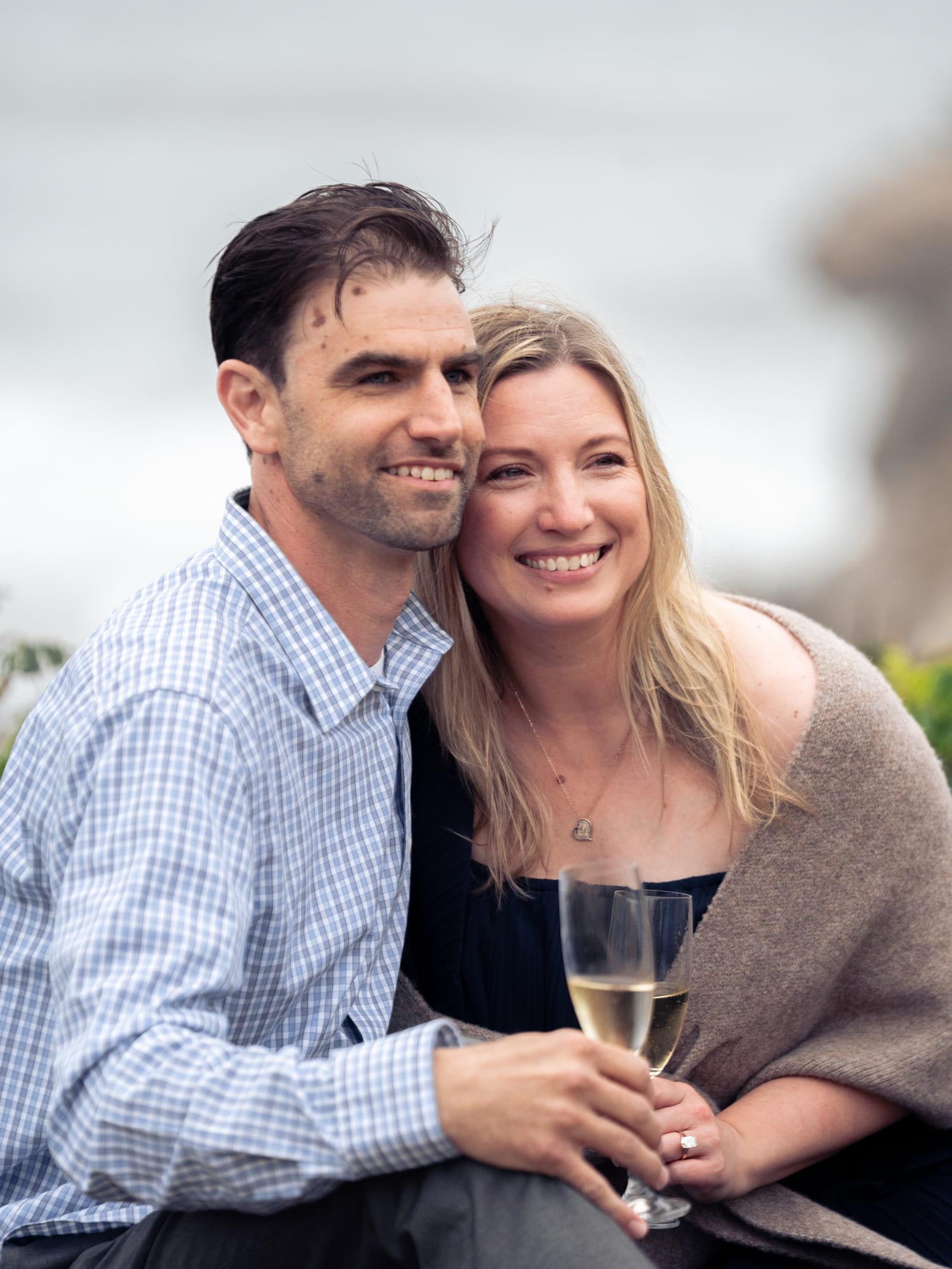 Close portrait of the couple forehead to forehead, her new engagement ring catching the light on her champagne glass