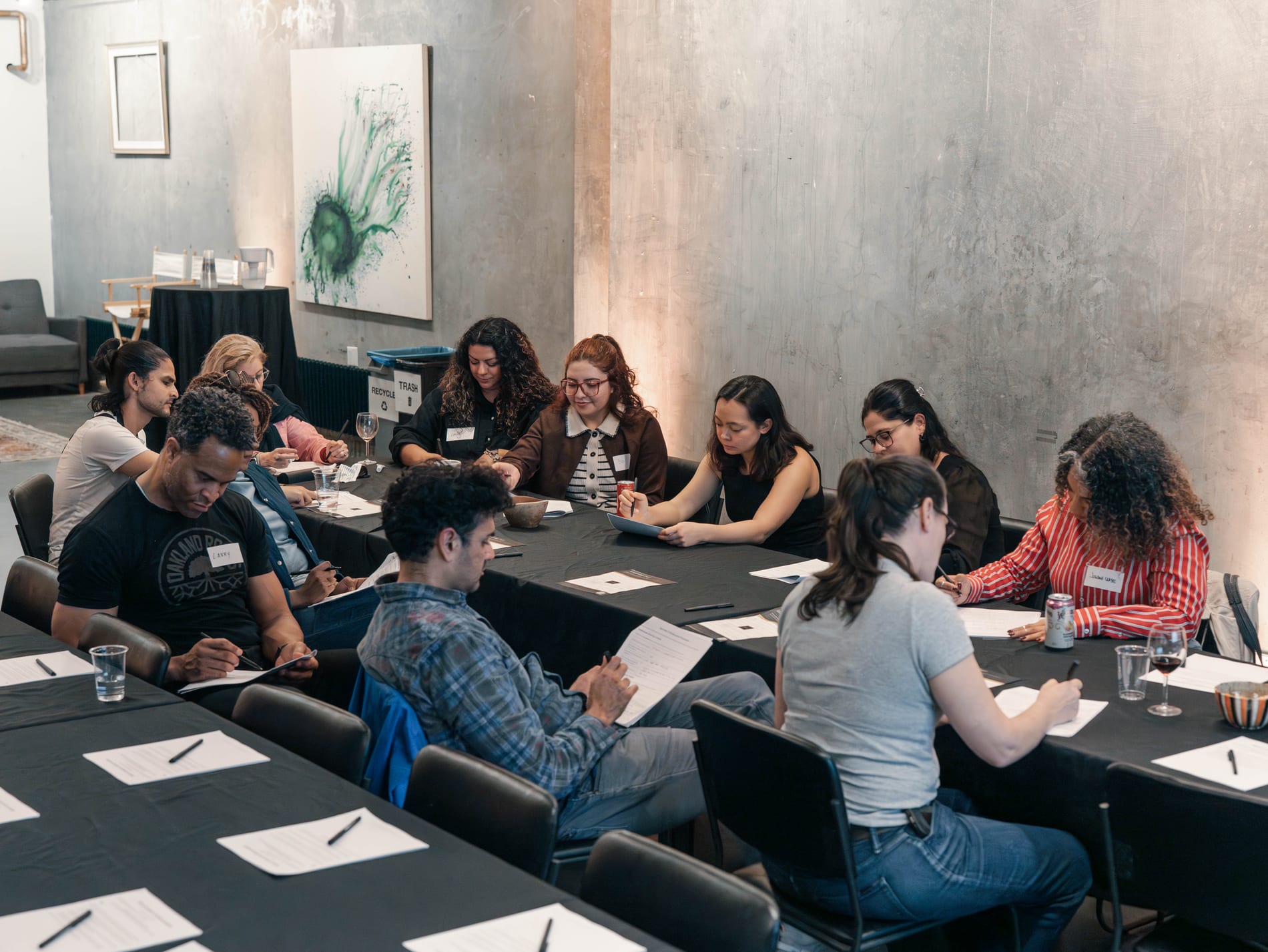 Guests fill out worksheets around an L-shaped table beneath an abstract green painting