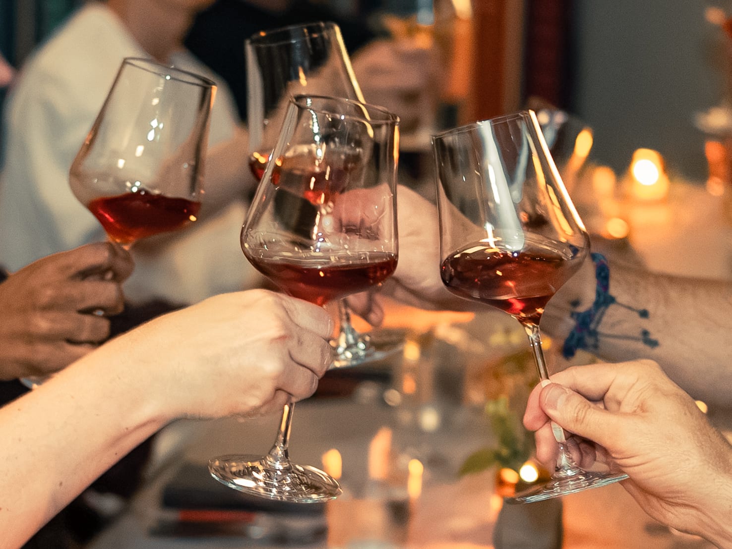 Four wine glasses clink together over a candlelit table as guests offer a toast
