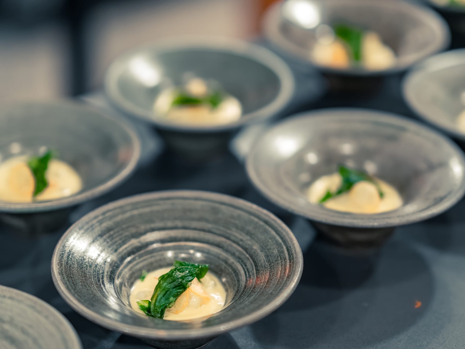 Small glass bowls of soup, each garnished with a single mint leaf, arranged across the table