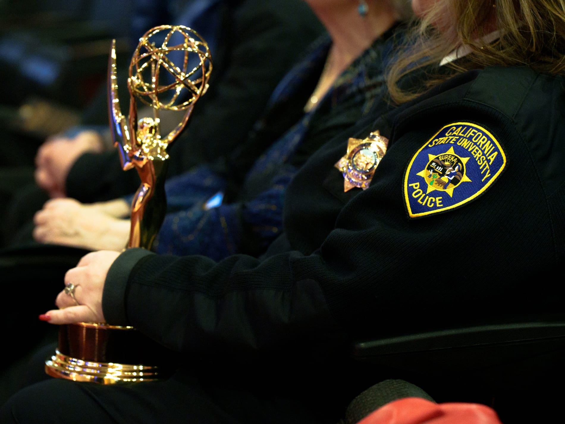 A seated guest in a California State University Police uniform holds an Emmy statuette in her lap during the ceremony