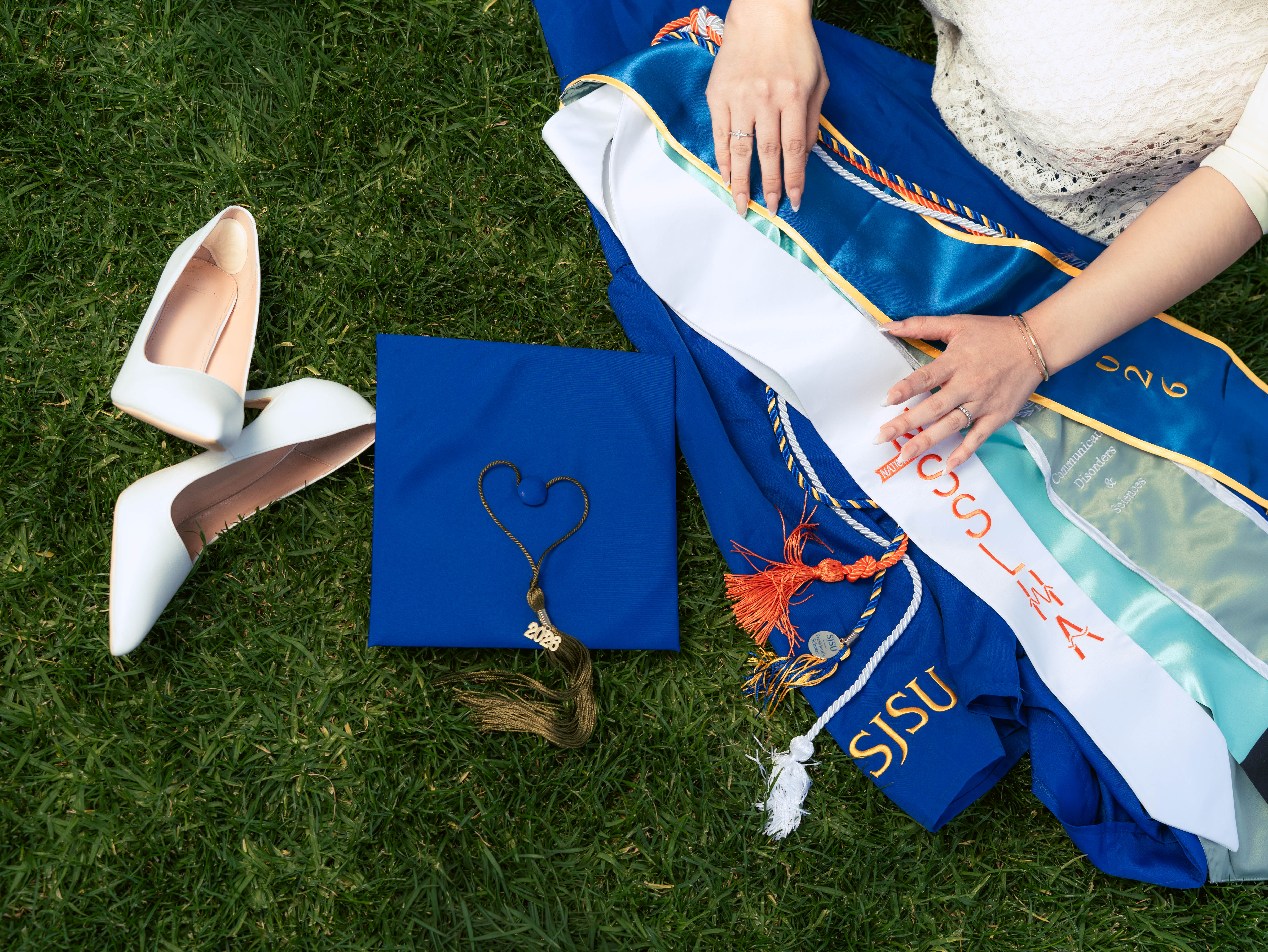Graduation cap, heels, and honor cords laid out on the grass at San Jose State