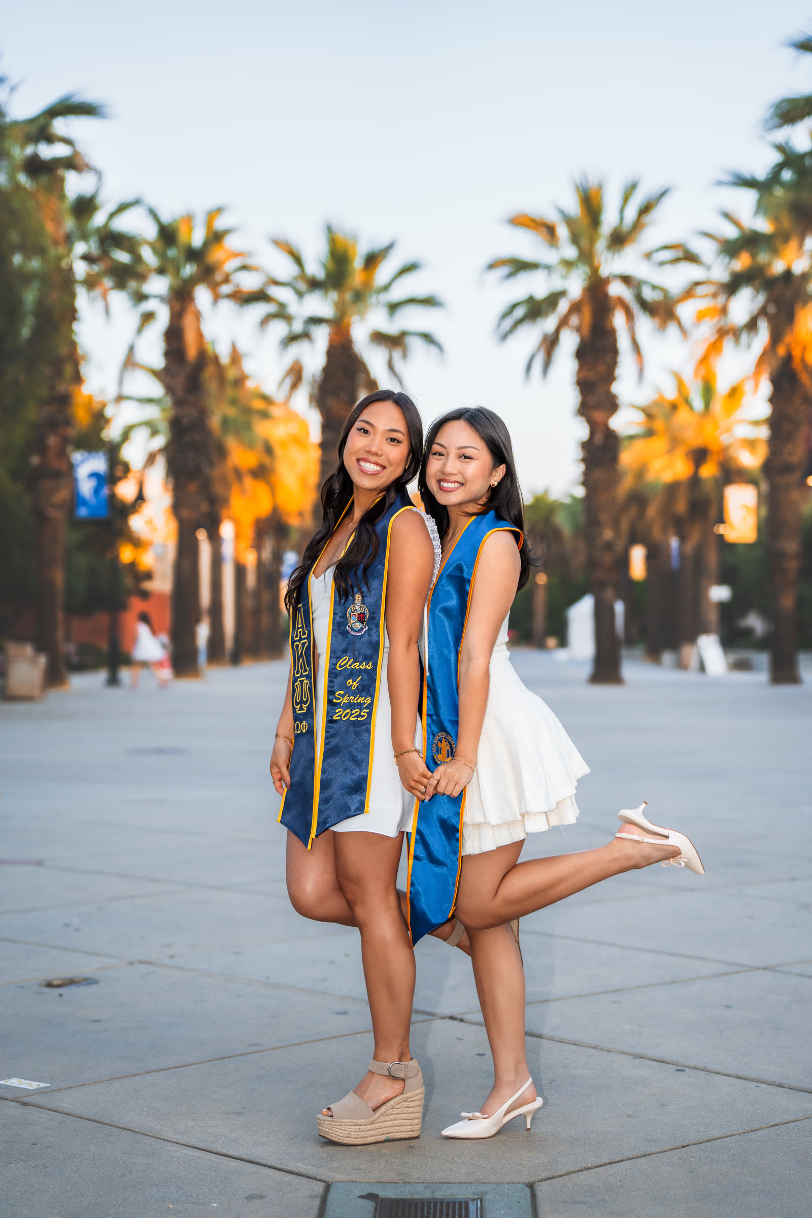 SJSU graduate posing on the grass with her cap, gown, and cords laid out around her