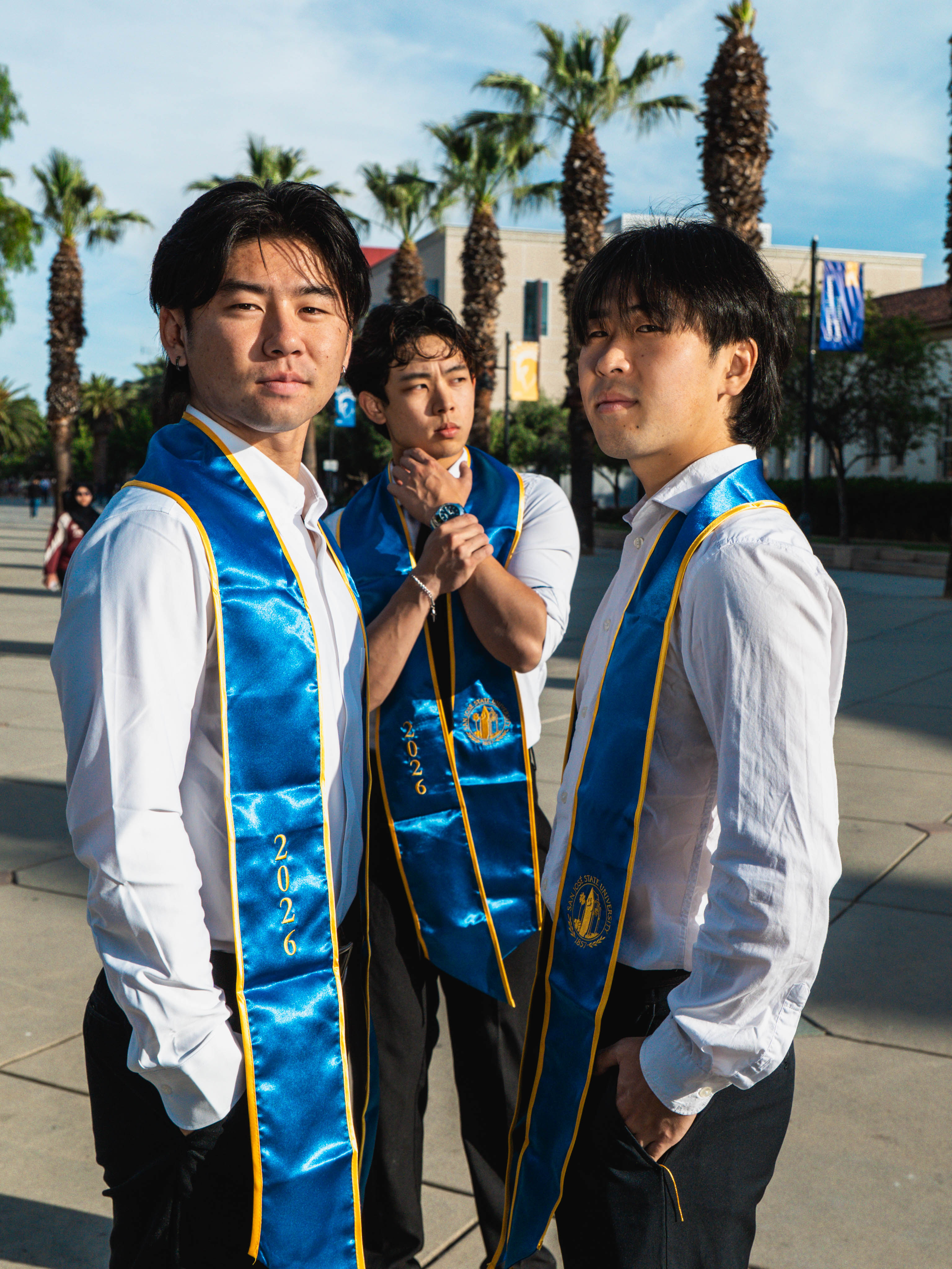 Three San Jose State fraternity brothers in graduation stoles posing together on campus