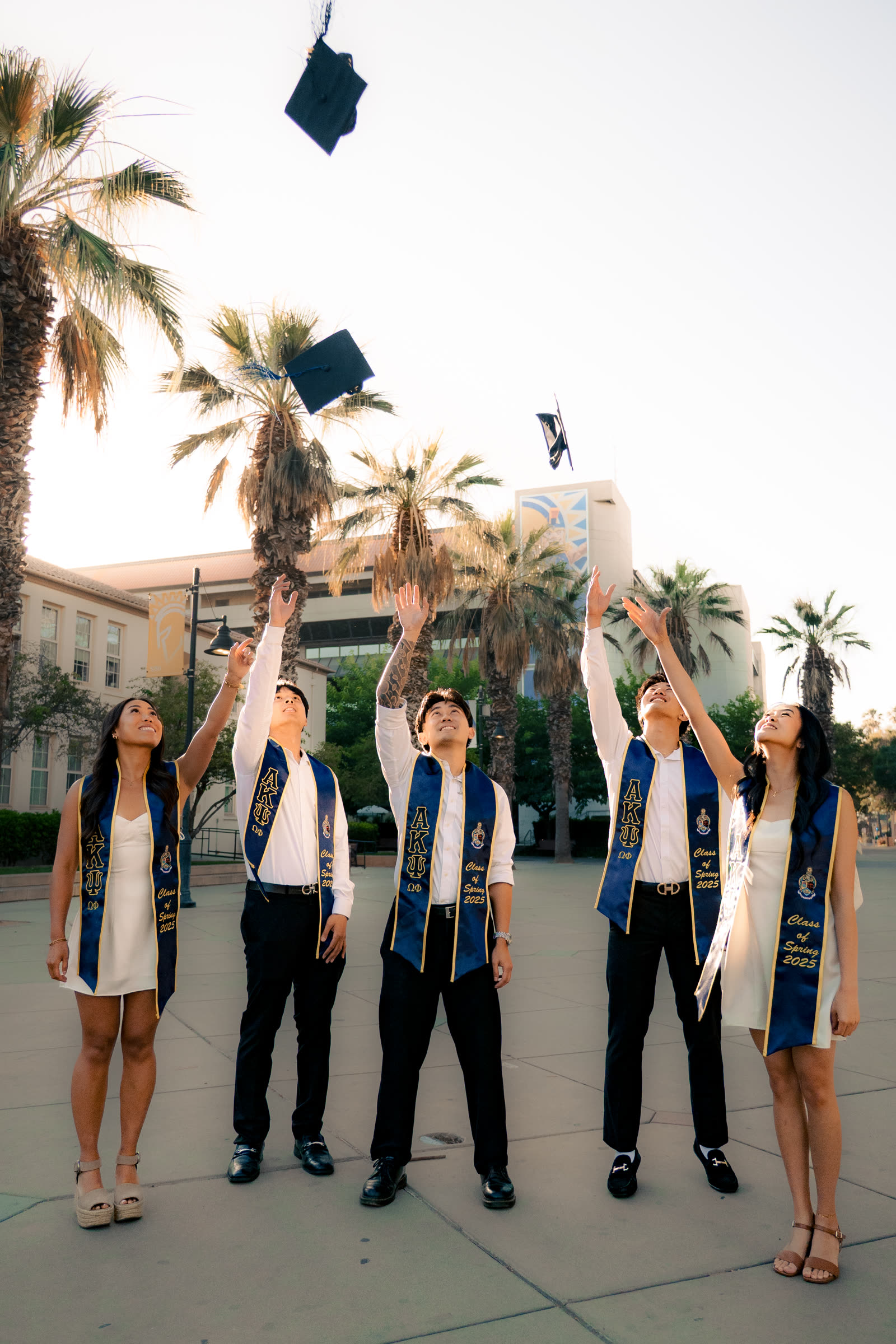 Five San Jose State graduates tossing their caps in the air on campus