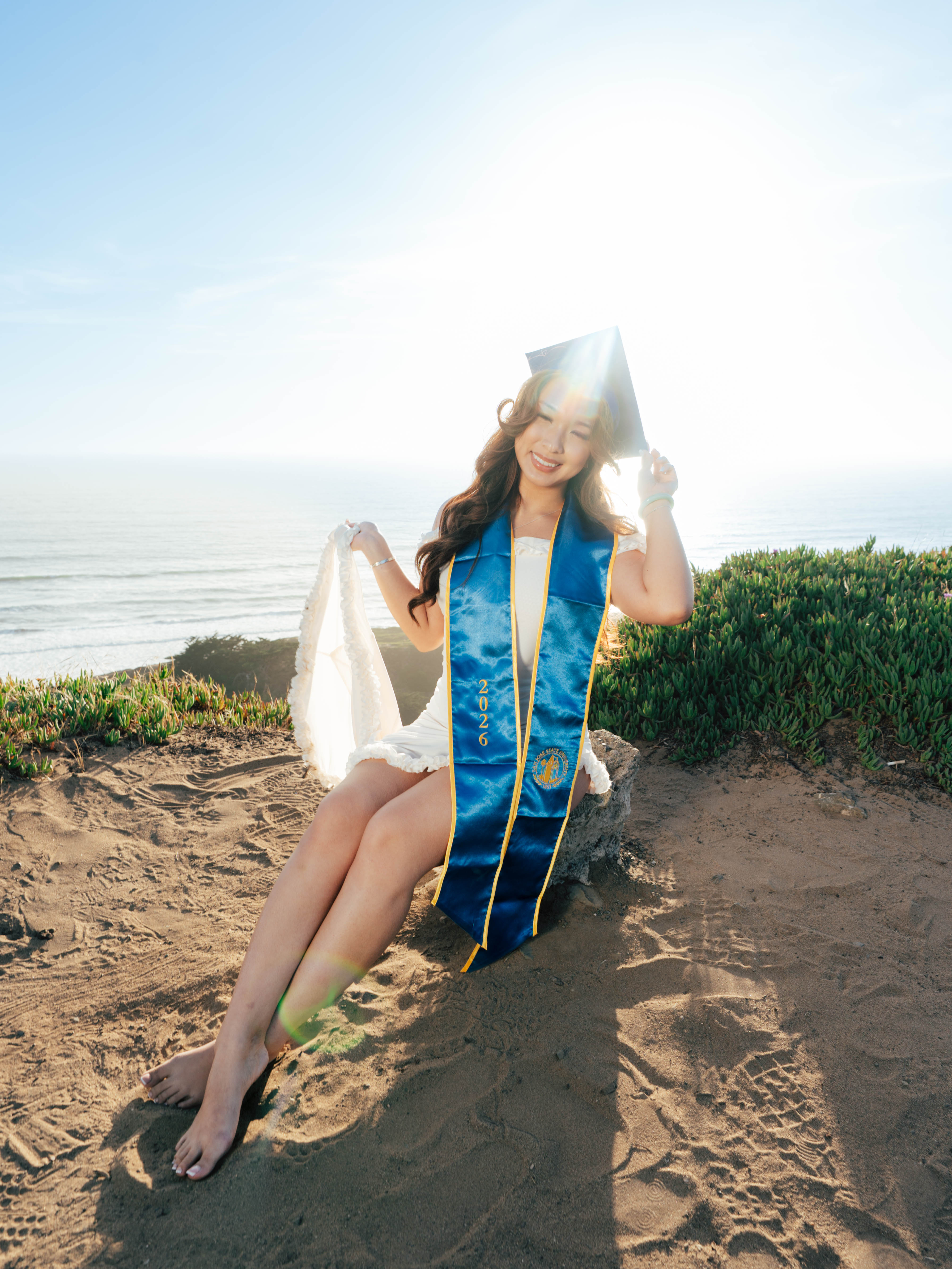 San Jose State graduate in her cap and gown on a bluff overlooking the coast