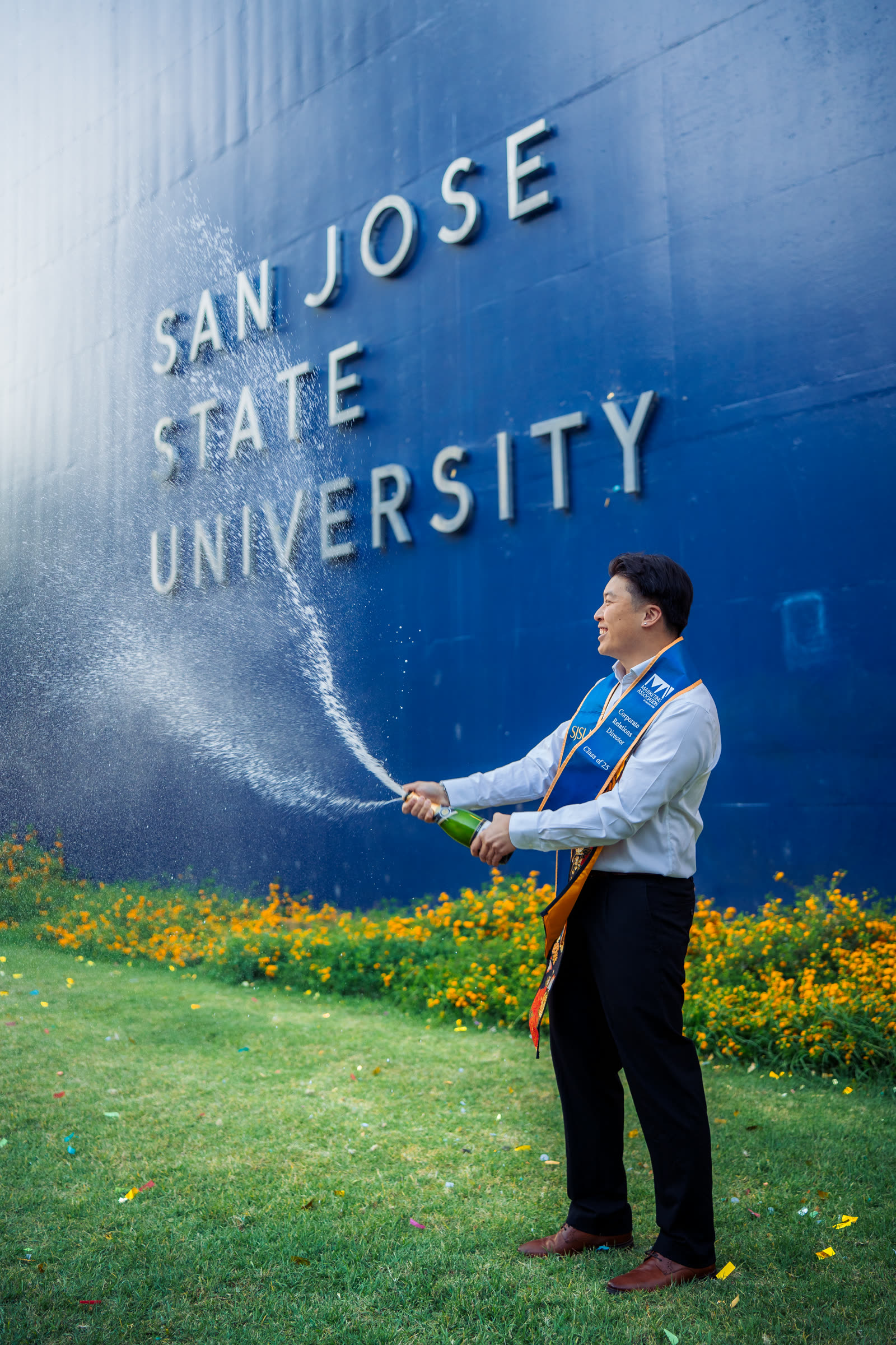 SJSU graduate popping champagne in front of the San Jose State University sign