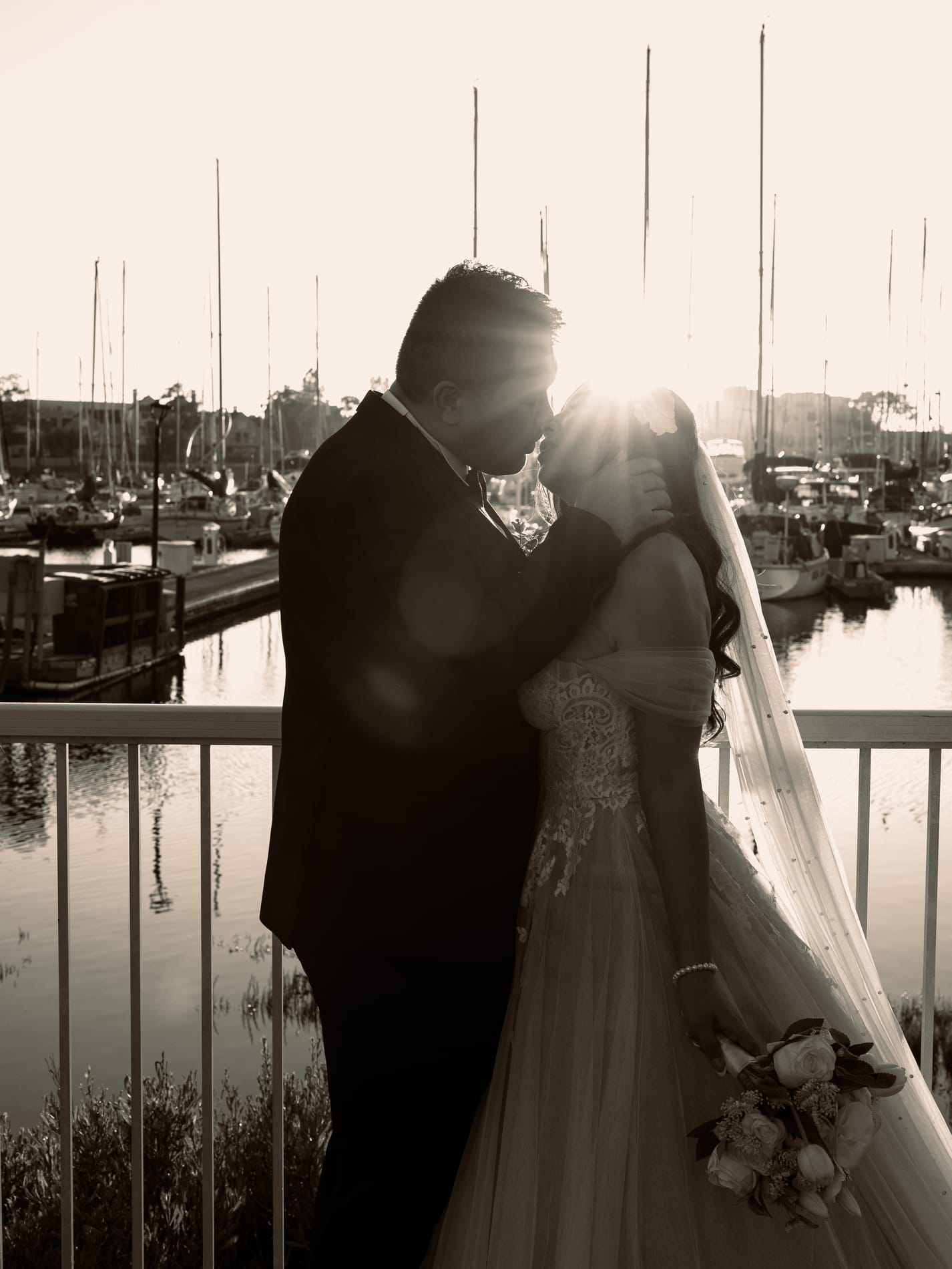 Bride and groom forehead to forehead in sepia, the sun flaring behind her veil