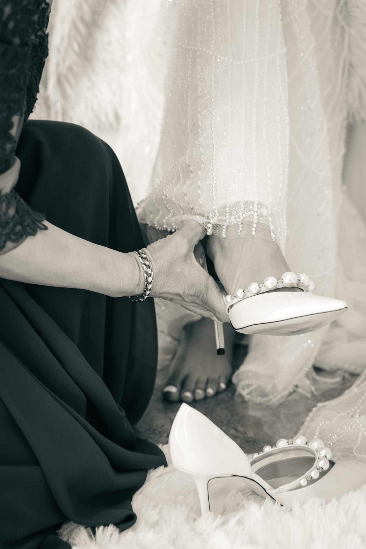 Hands fastening the bride's pearl-studded heel while the second shoe waits on the rug, sepia