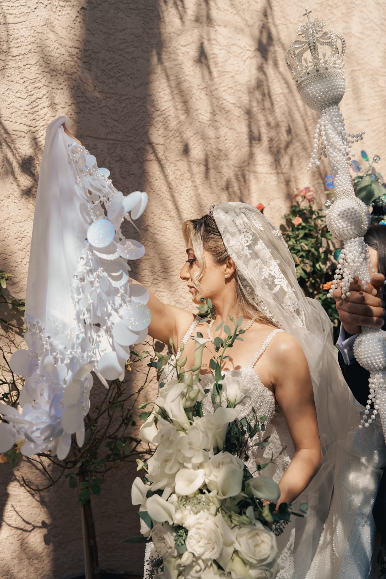 Bride in profile beneath her lace veil beside the beaded ceremonial fan and scepter