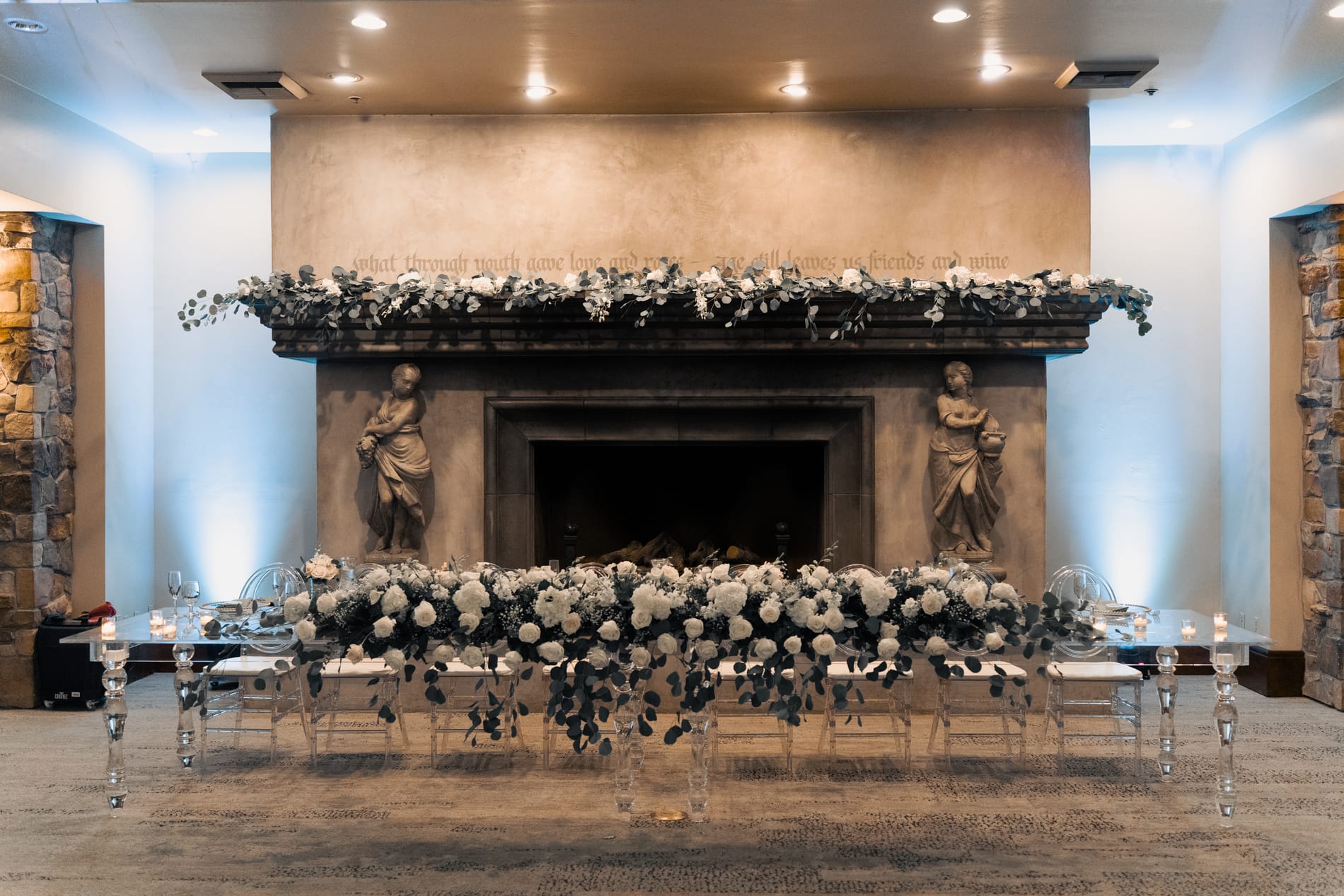 Head table set in front of the reception fireplace, banked with white roses and eucalyptus