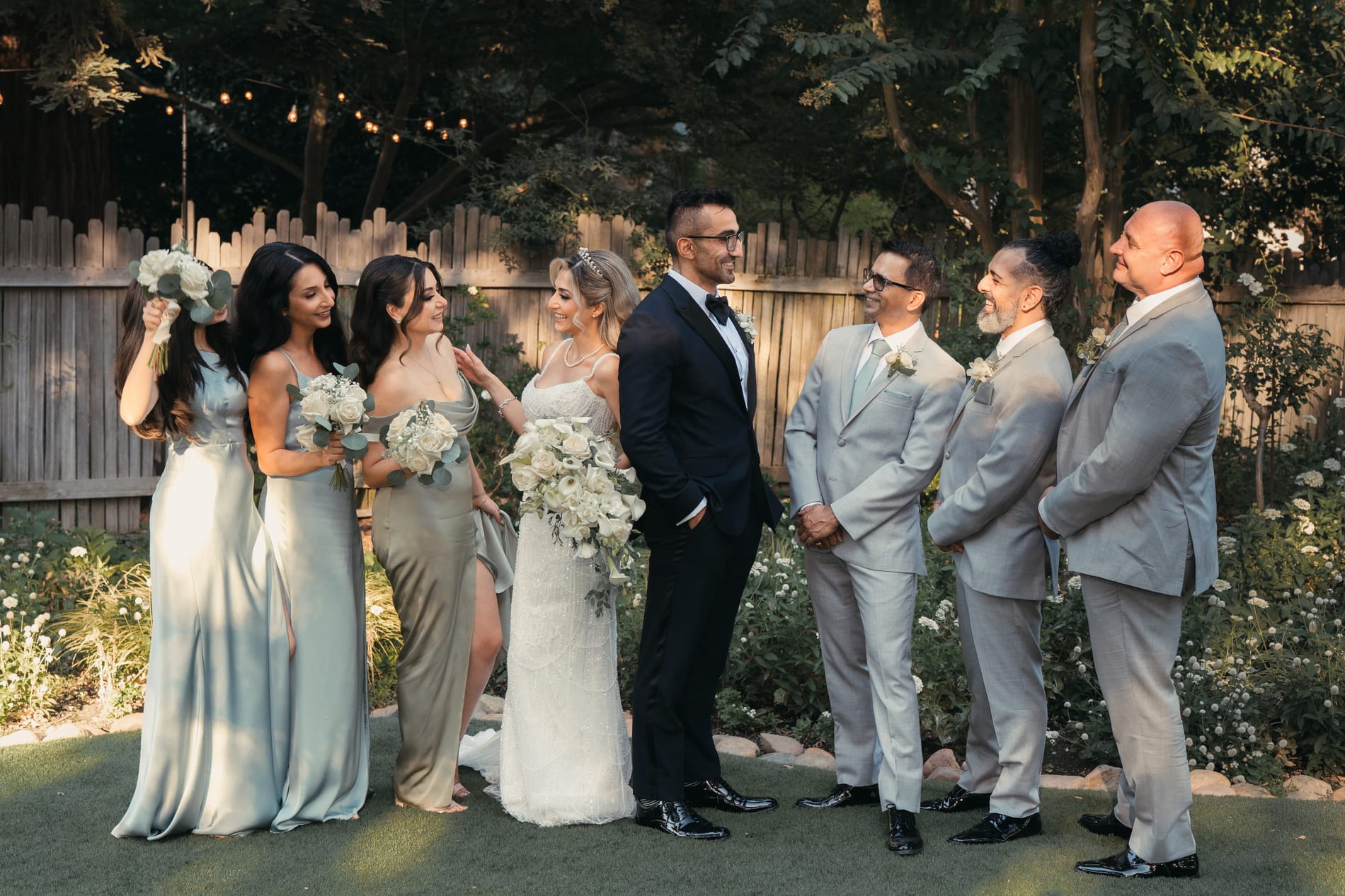 The wedding party lined up in the garden at golden hour, bridesmaids in sage and groomsmen in grey