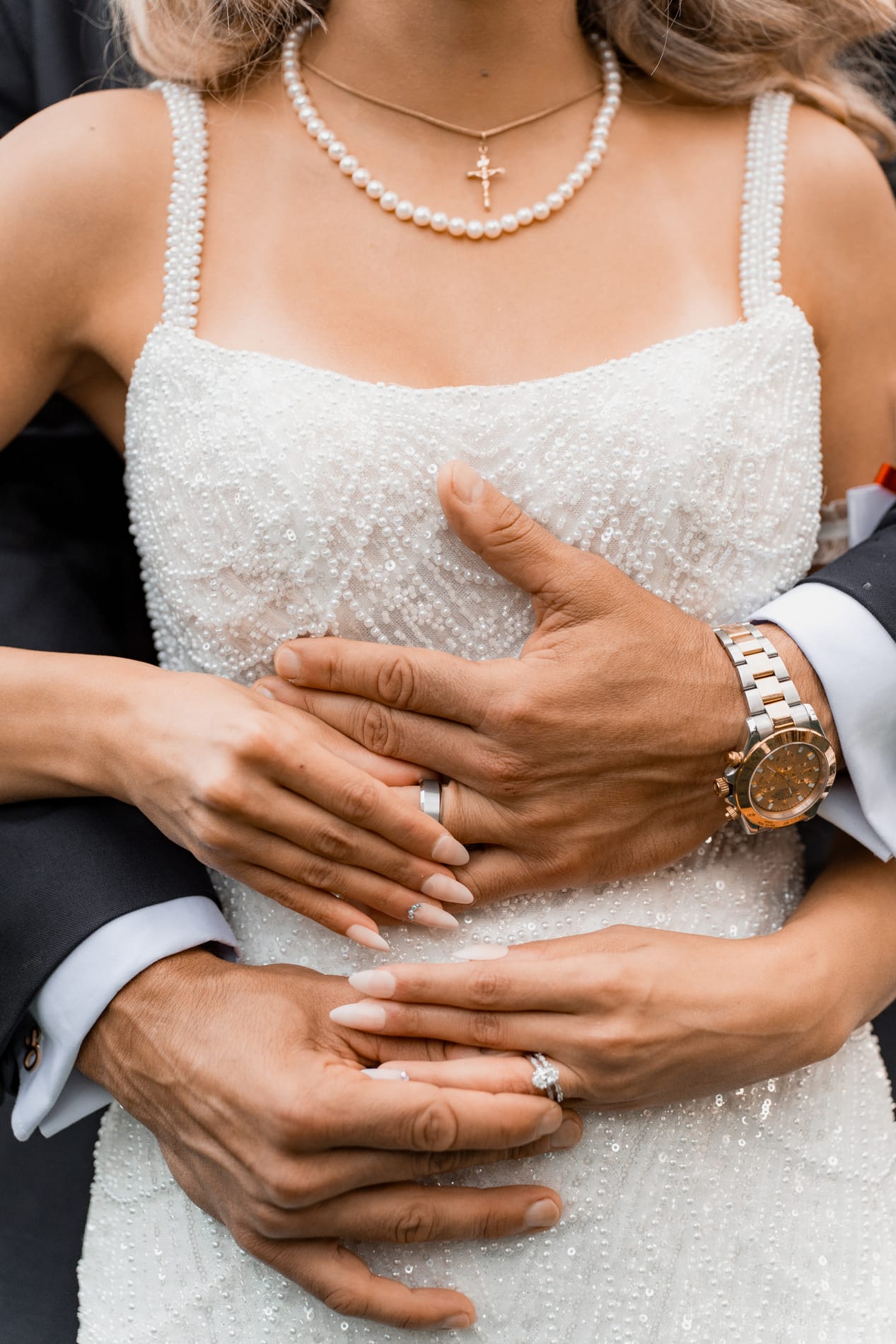 Groom's arms wrapped around the bride's beaded gown, both wedding bands showing