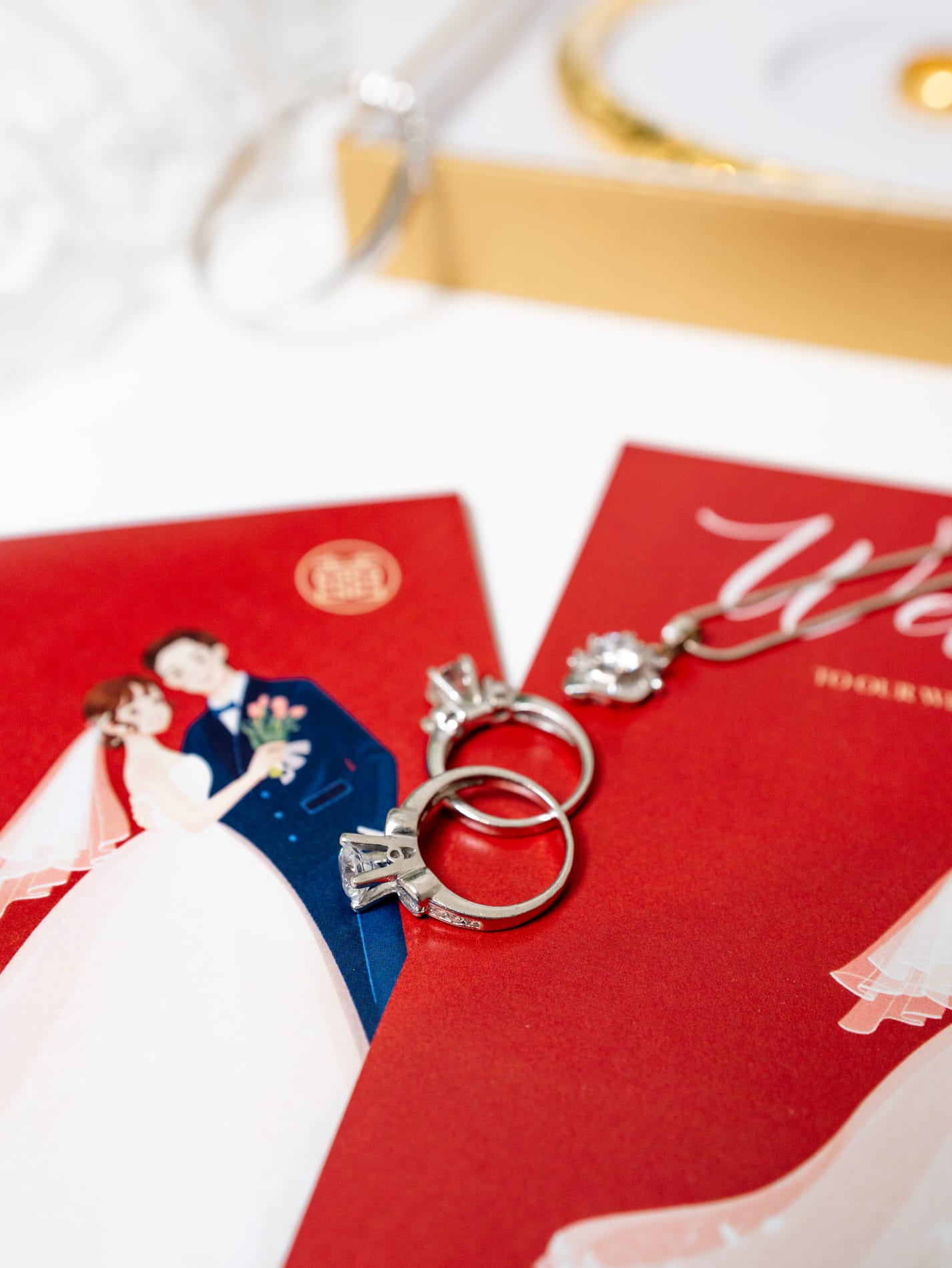 The wedding bands and earrings resting on a red invitation illustrated with the couple