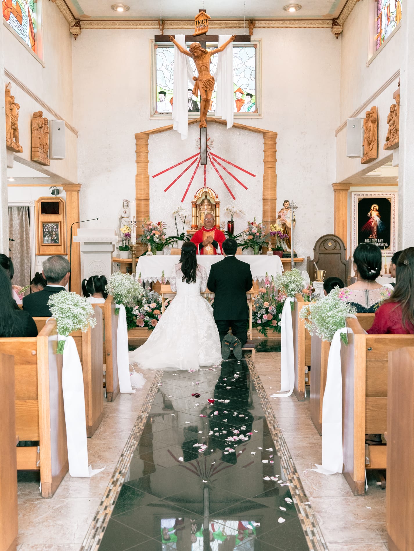 Bride and groom at the altar seen from the back of the church, petals scattered down the aisle