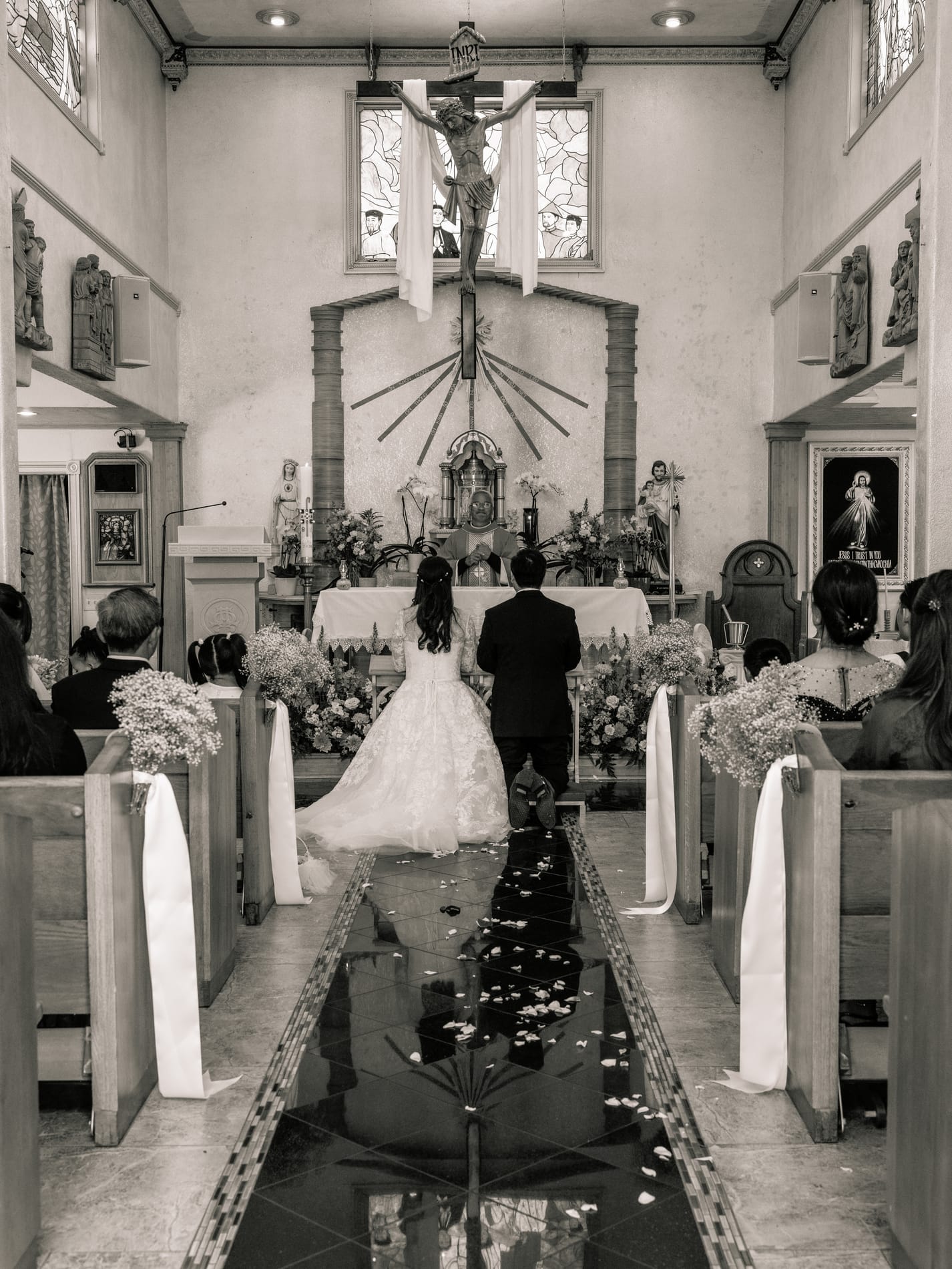 Bride and groom at the altar seen from the back of the church, petals scattered down the aisle, black and white
