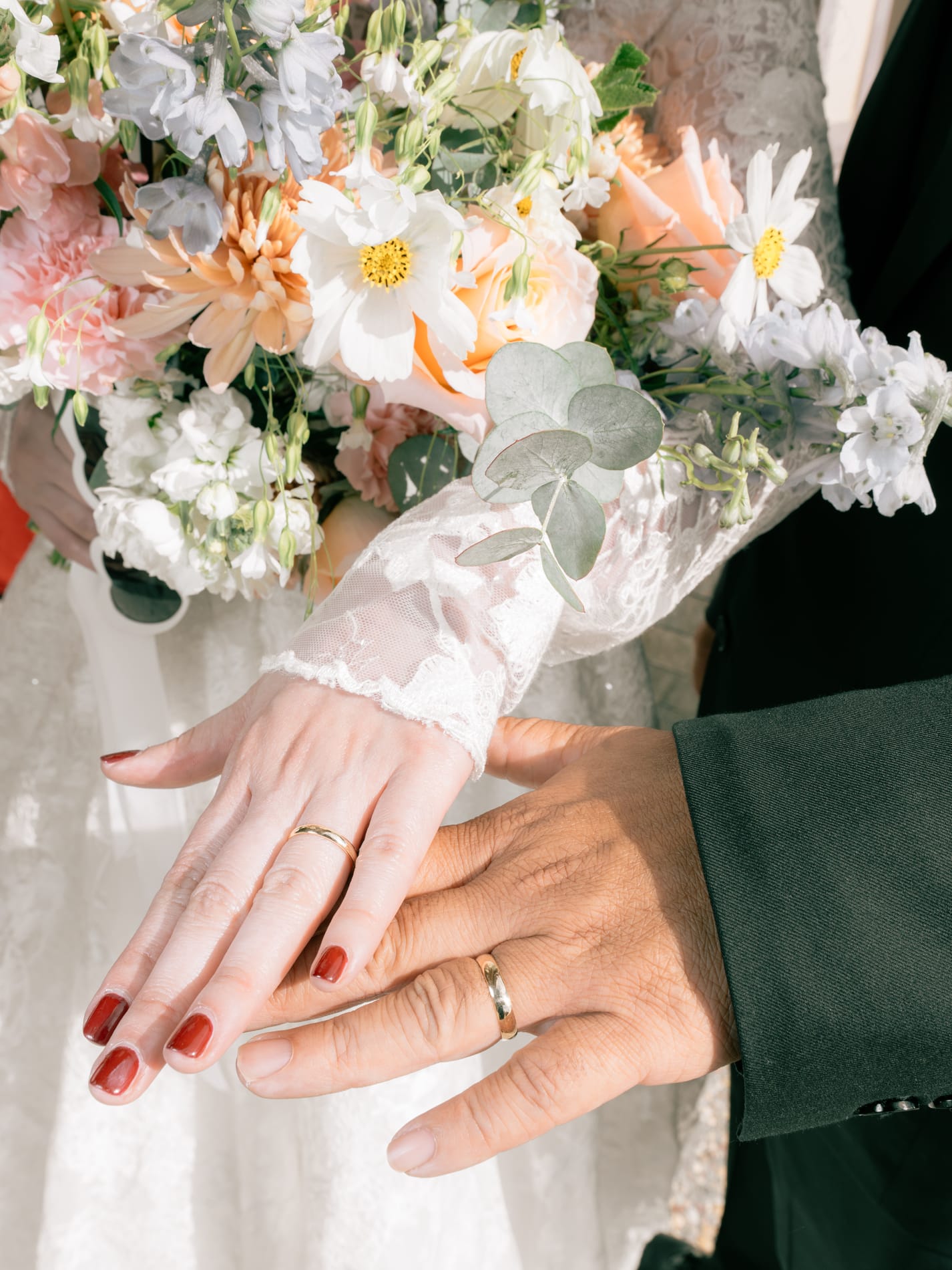 The couple's hands resting together over the bouquet, both wedding bands on