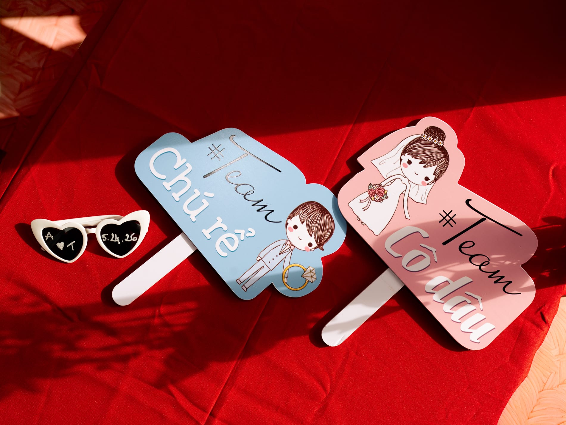 Paddle fans for the bride's side and the groom's side laid out with heart sunglasses on a red reception table